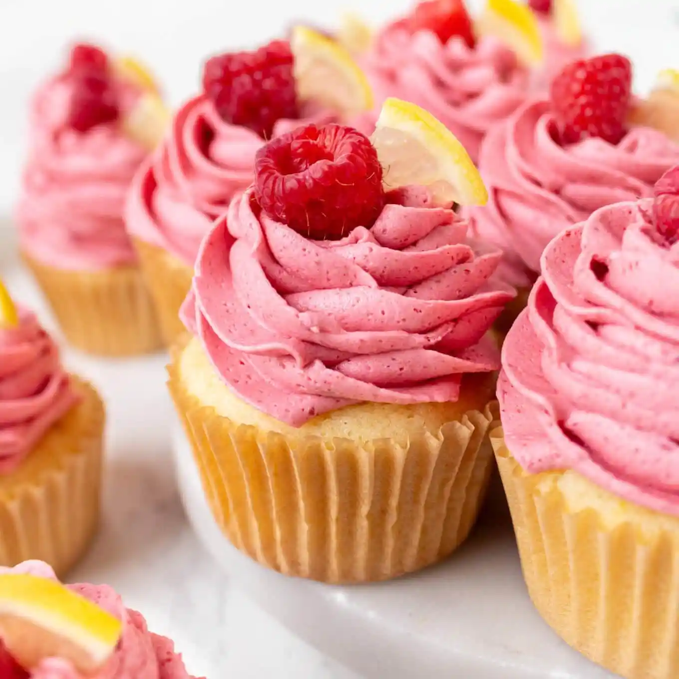 Pink frosted cupcake with a swirl of icing, topped by a raspberry and a lemon wedge on a vanilla cupcake base.
