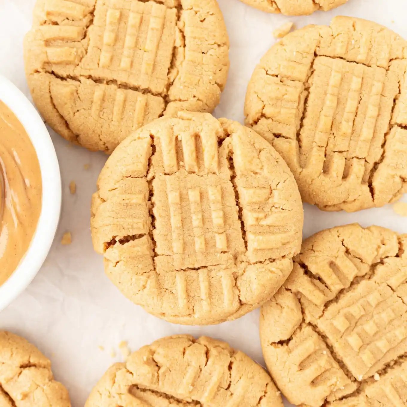 Pile of peanut butter cookies with fork-score crisscross pattern on parchment.